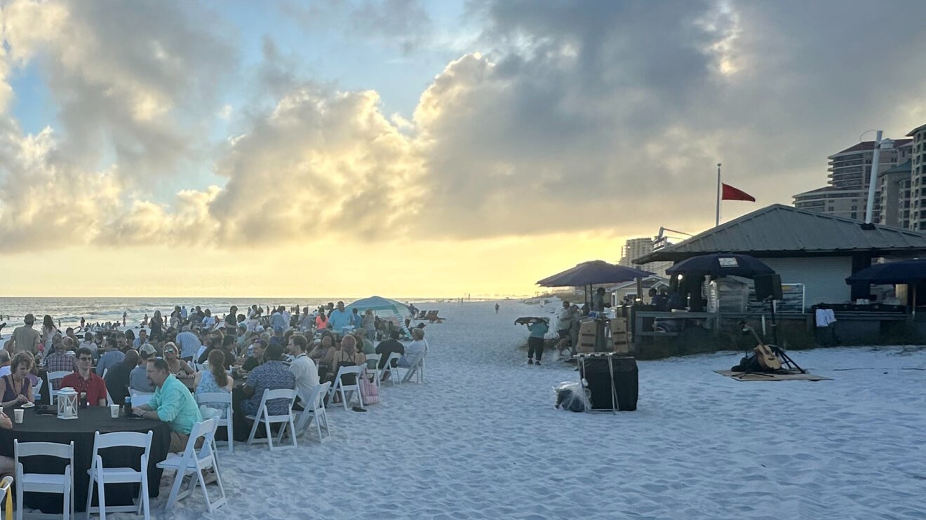 Attendees at long tables on the beach at sunset during the EUG 2026 beach dinner in Sandestin, Florida
